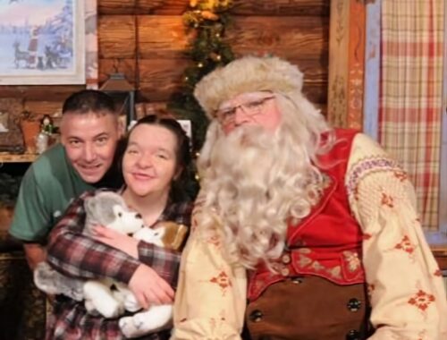 A father leans over the shoulder of his daughter who is sat next to Santa