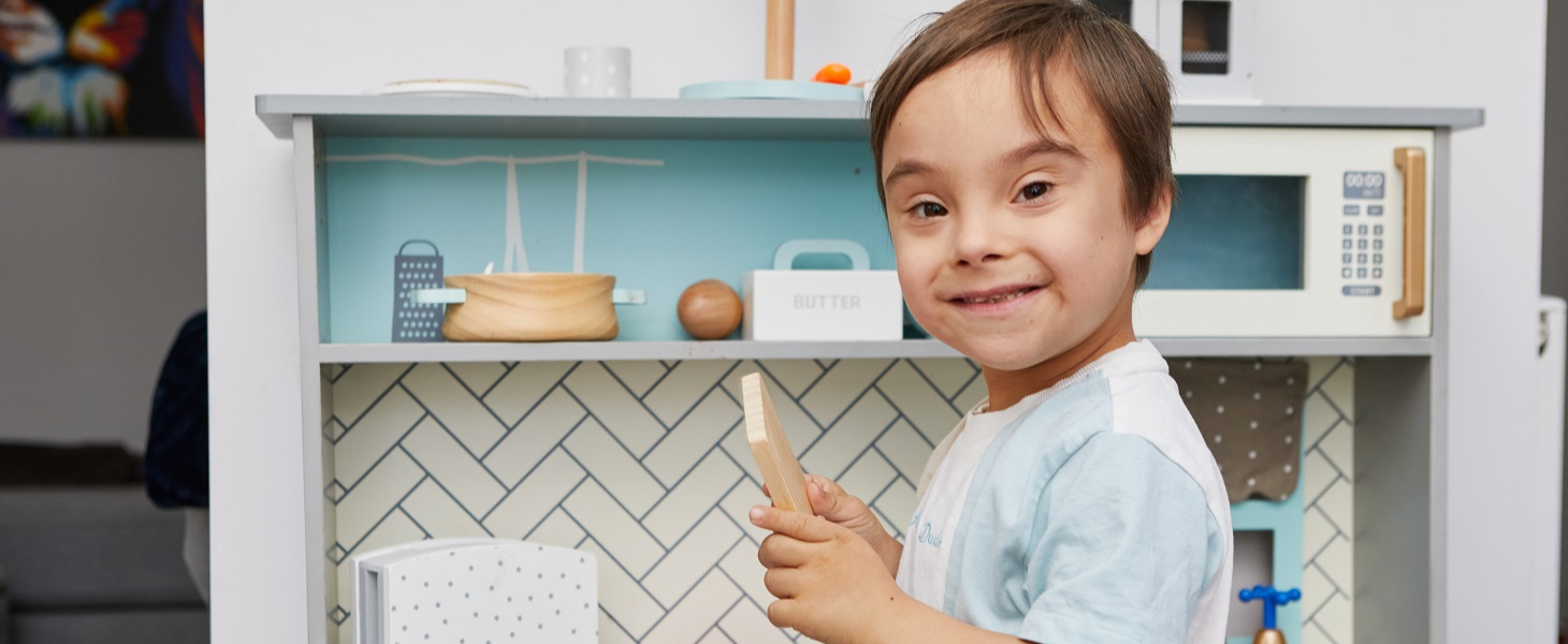 A little boy holds a fake piece of bread while playing in his toy kitchen