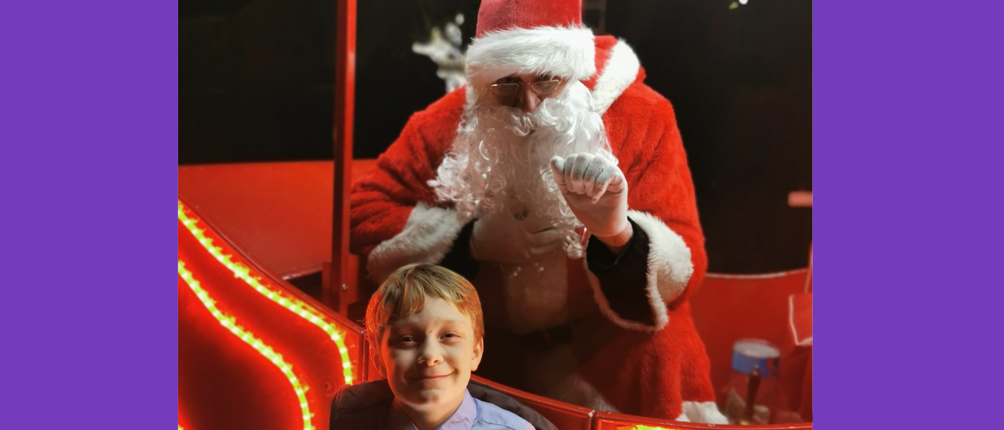 Little boy stands in front of Father Christmas, smiling for a photo.