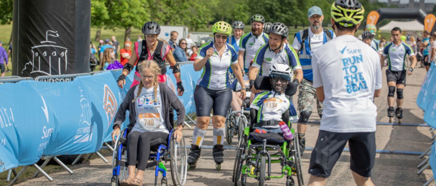A group of event participants about to cross the finish line at Parallel Windsor. Two people are in wheelchairs and some on roller blades behind them