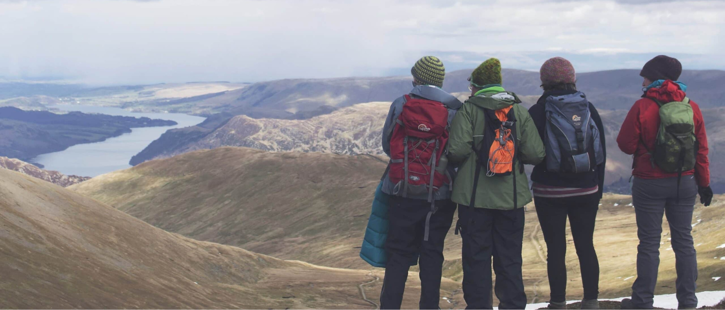 A group of four people in coats and hats stood at the top of a mountain looking at the views below