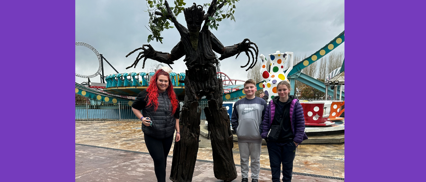 Three siblings stand in front of a sculpture of a tree and smile at the camera.