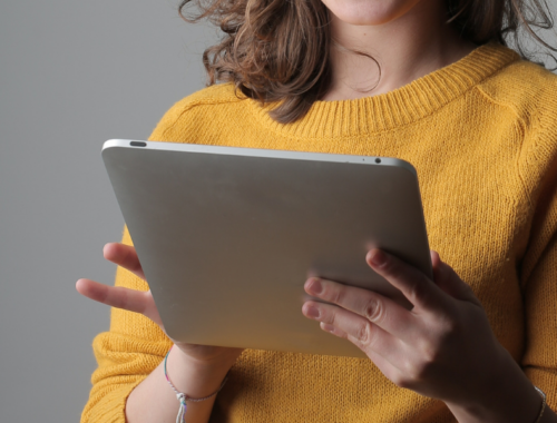 A woman wearing a yellow jumper holds an iPad in her hands