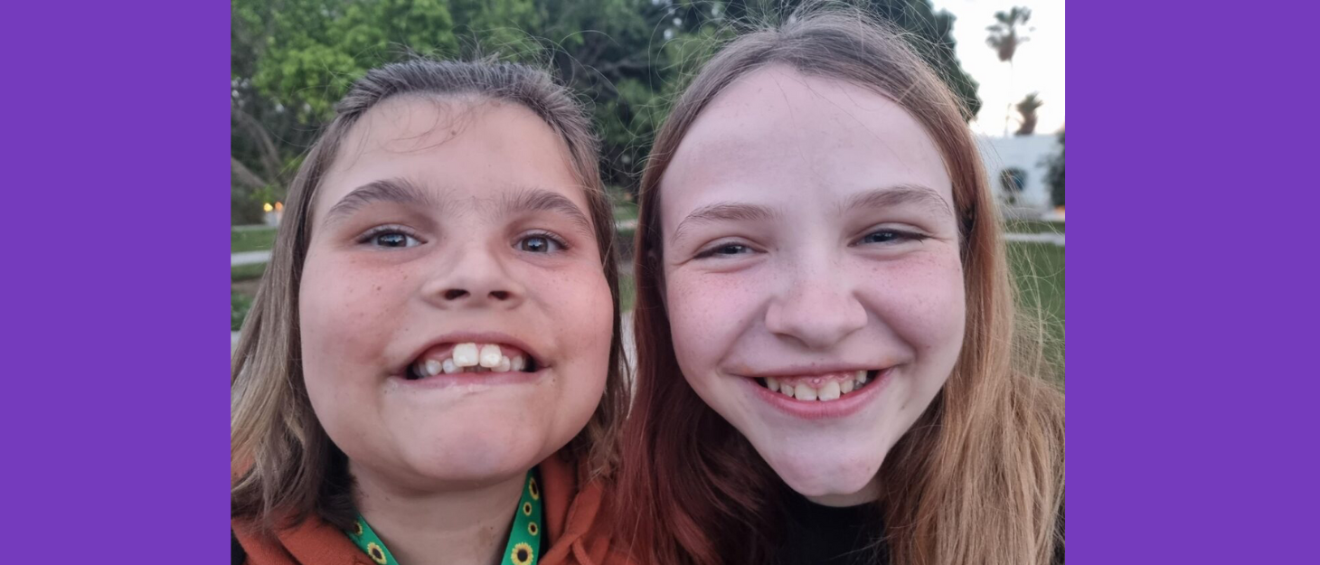 Two sisters take a selfie, grinning at the camera. One sister wears a sunflower lanyard.