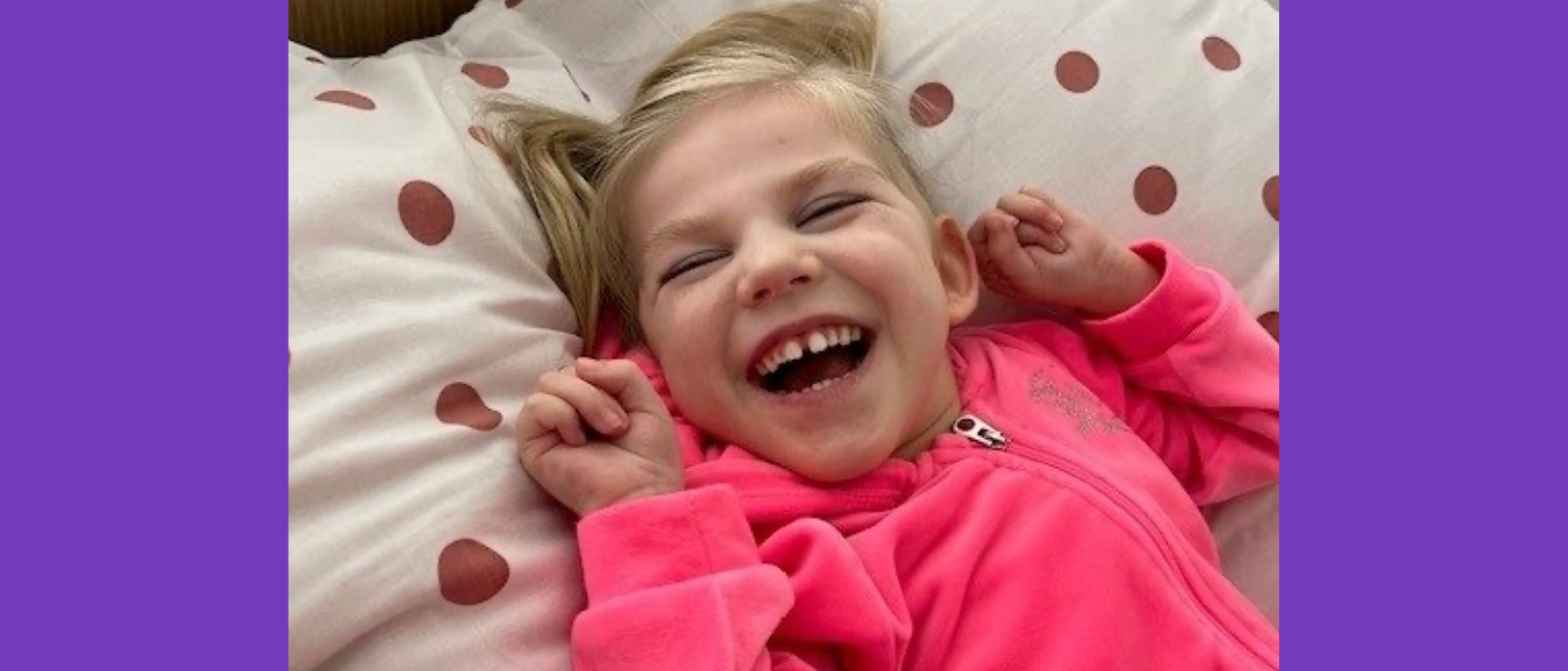 Little girl wearing pink hoodie lies on her bed smiling for the camera