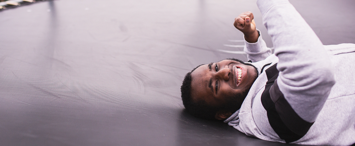 A young man lies on a trampoline. He is smiling.