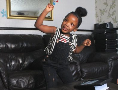A young girl dancing in her living room wearing a stripped top and dungarees