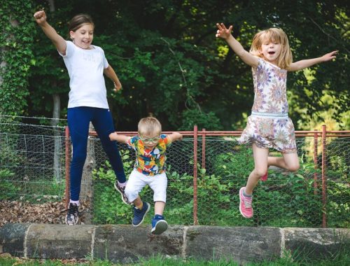 Three siblings, two girls and a boy in the middle, playing outside jumping into the air with their arms up