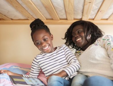 A young girl and her mum smiling, sat together on the bottom bunk bed, looking a tablet