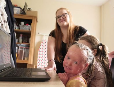 A mum and her two daughters sat at a kitchen table looking at a computer