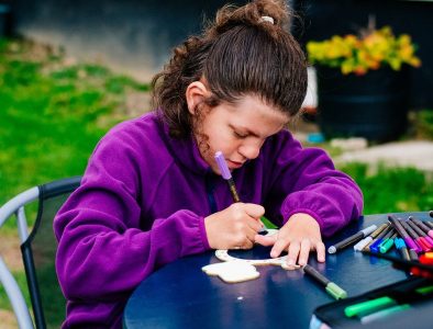 A young girl in a purple fleece, using colouring pens at a table in the garden