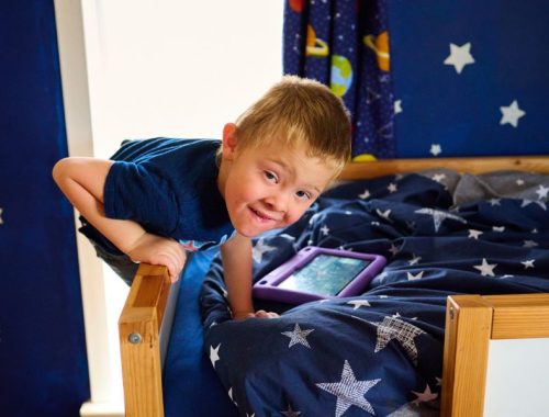 Little boy in a blue bedroom, climbing onto a bunk bed with his tablet