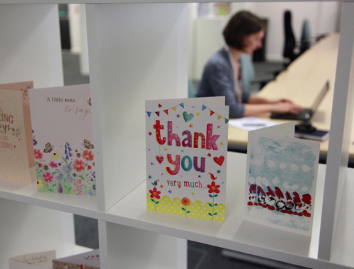 Thank you cards arranged on white shelves. In the background, a woman works on a laptop