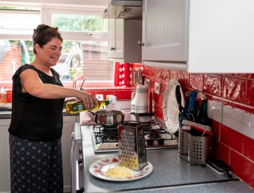 A mother cooking in a red tiled kitchen, pouring oil into a pan on the hob