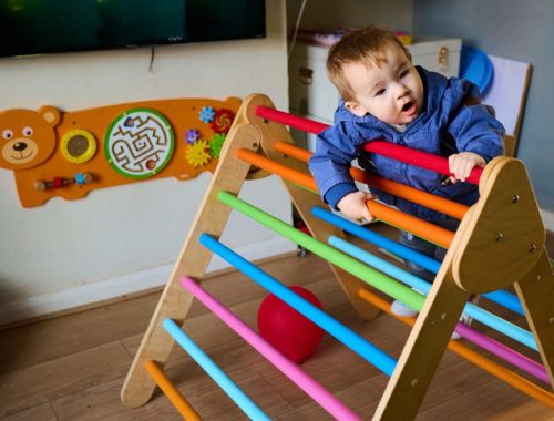 A toddler climbing on a brightly coloured sensory toy in the living room