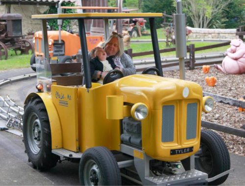 A toddler on his grandmothers knee, riding in a yellow tractor atomtronic ride at an adventure park