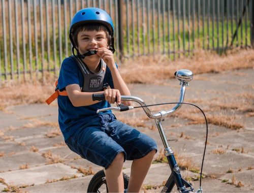 A boy in denim shorts, t-shirt and blue helmet riding a bike