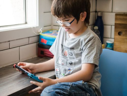A boy with glasses playing on a handheld games console