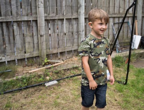 Boy with hearing aid standing in front of a football net in the garden