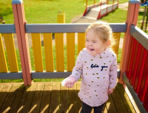 A little girl in a pink hoodie standing on a platform at an adventure park