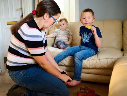 Mother putting on socks and shoes on her son who is eating an ice lolly
