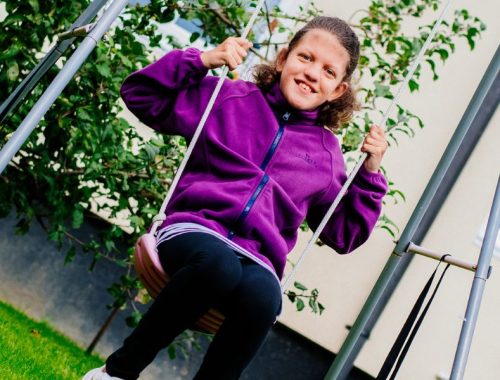 A girl wearing a purple fleece on a garden swing