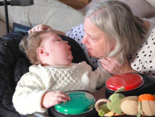 Toddler with his hands on a green push button, looking at his grandma