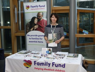 A Family Fund representative is at an events with a table in front of her with Family Fund information and leaflets on