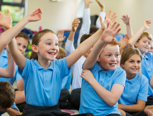 A group of children wearing school uniforms smiling and raising their hands