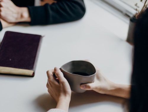 Hands holding a coffee mug over a white table that has a notebook on it