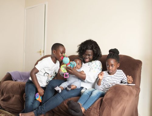 a mum and her three children sitting on a couch, playing and reading a book together