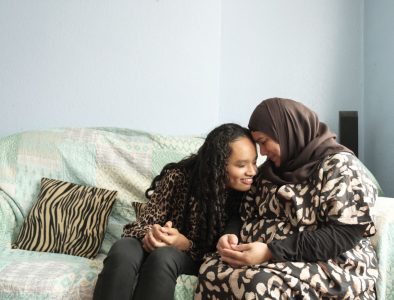 A mum and her daughter on a sofa, hugging and smiling