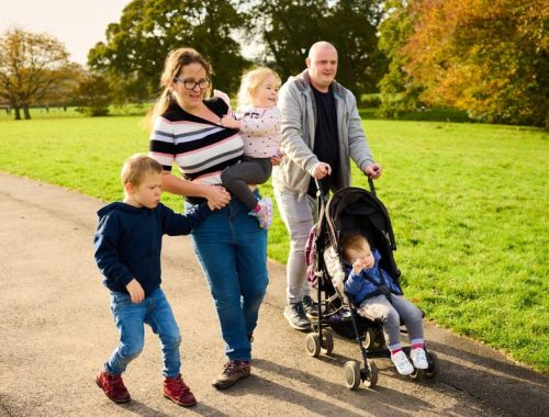 A mum and dad walk through a park with their 3 children