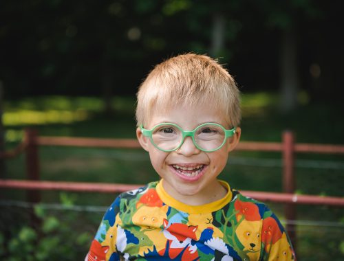 A boy wearing green glasses grinning at the camera