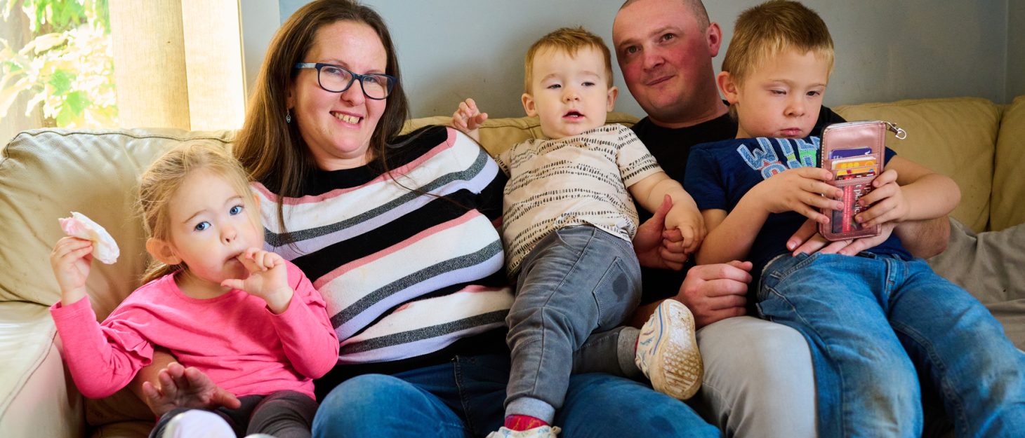 Family sitting on the sofa including mum, dad, young boy, young girl and baby boy.