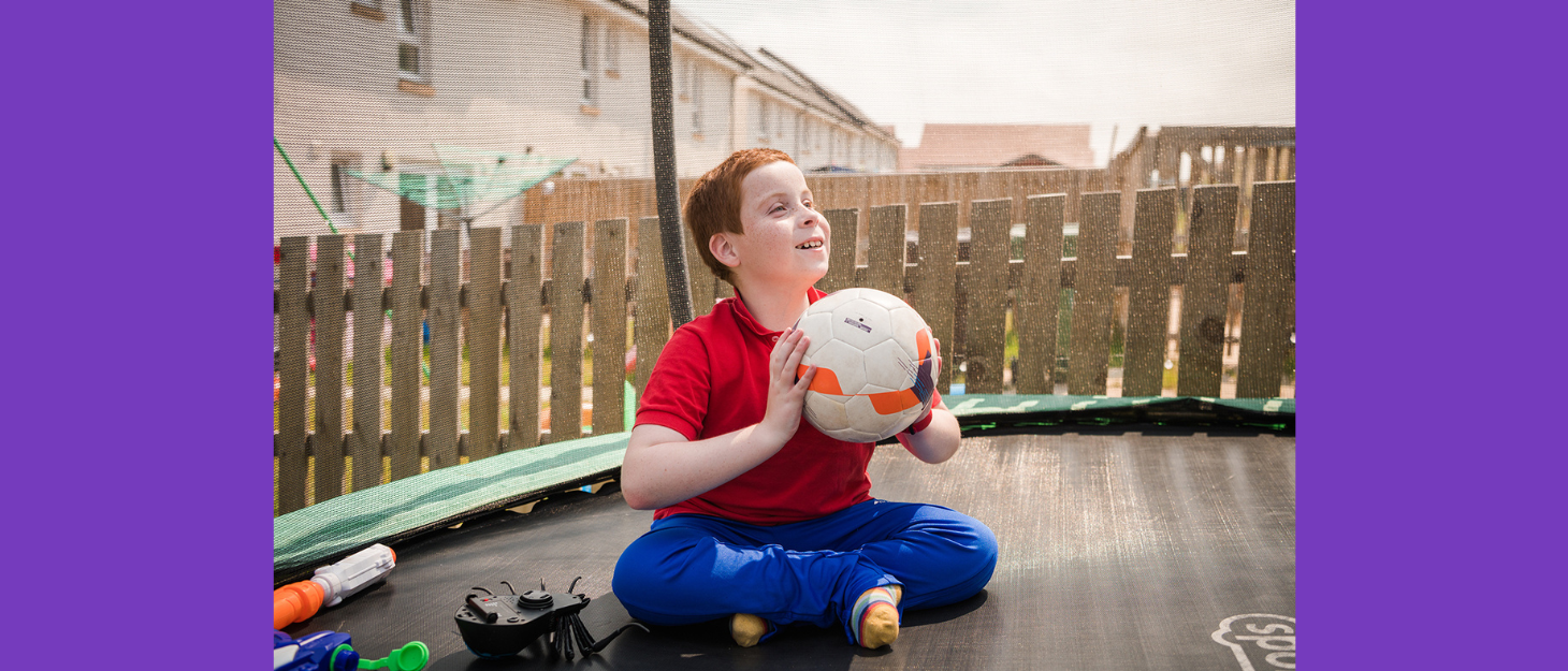 Boy sitting on trampoline about to throw a football