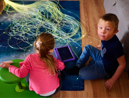 A little girl and her brother sitting on the floor playing with sensory toy string lights