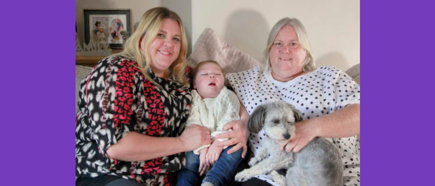 Baby is cuddled by his mum and his grandma, who is holding their dog