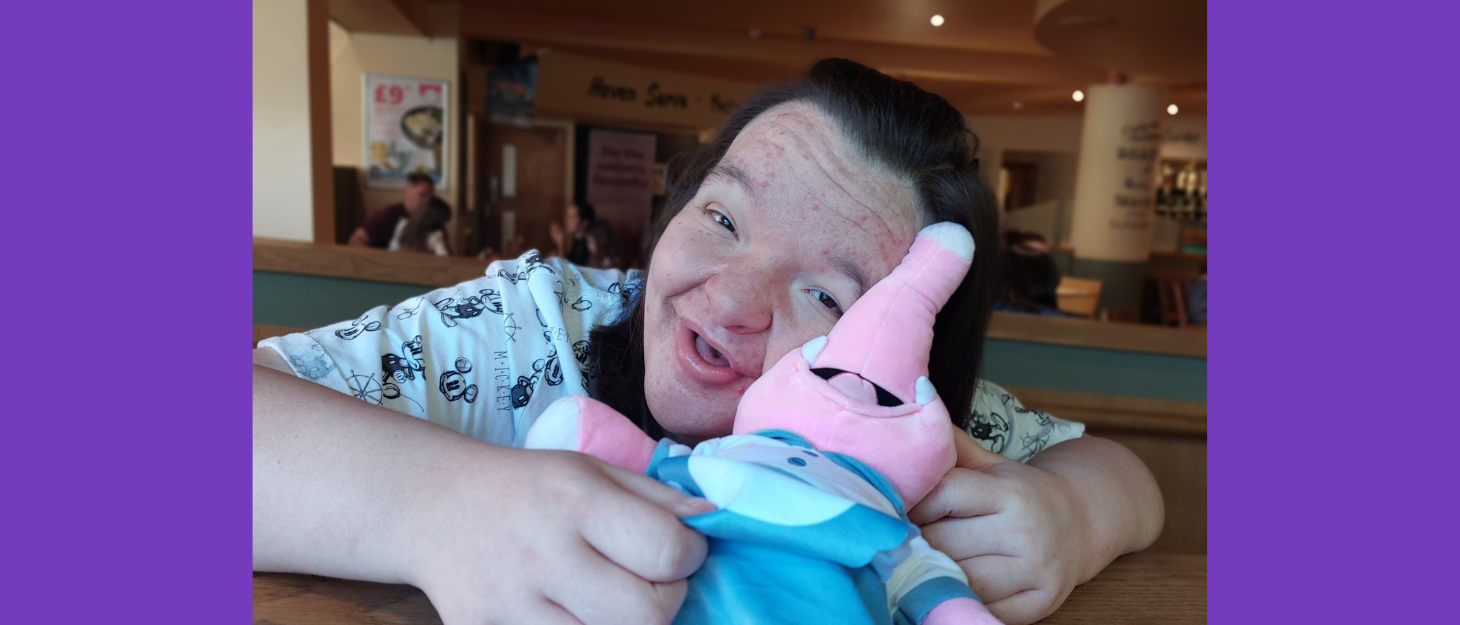 Young woman smiles at camera and holds a pink cuddly toy