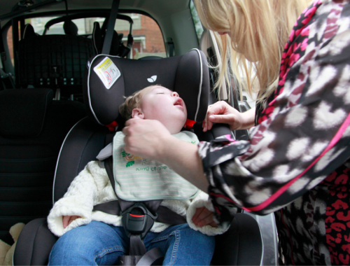 a mum putting her toddler safely in a car seat