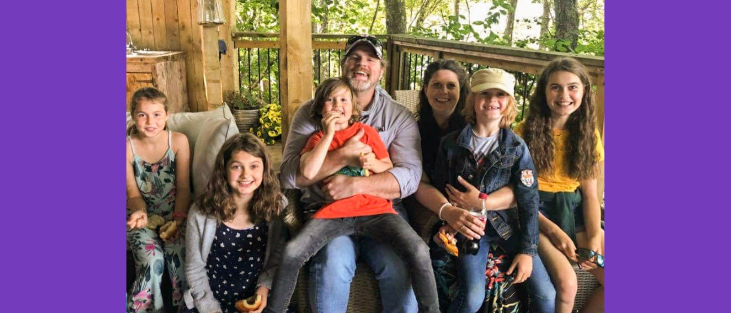 A mum, her husband, and their five children sit together smiling at the camera at a wildlife park