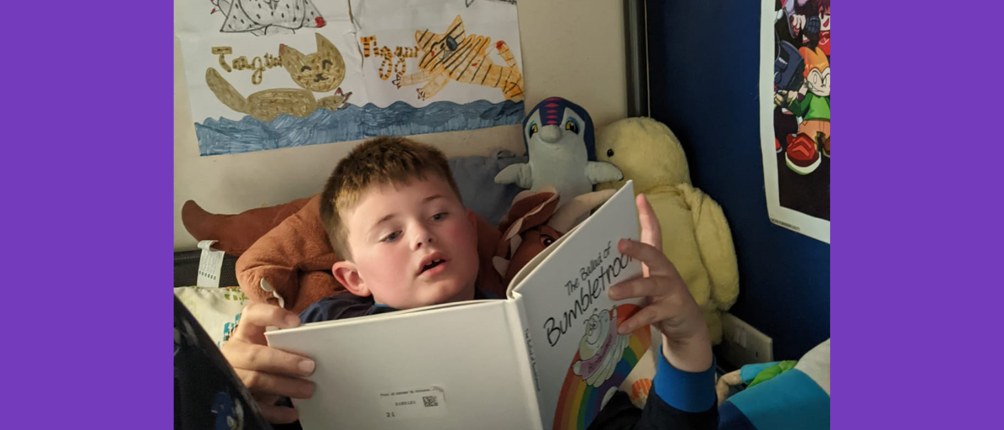 Boy lies in bed reading his book.