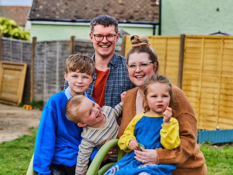 A family (mum, dad, two brothers and a sister) smile together in their garden.
