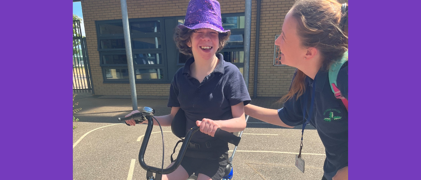 Girl riding specialist bike is helped by support worker and smiles at camera