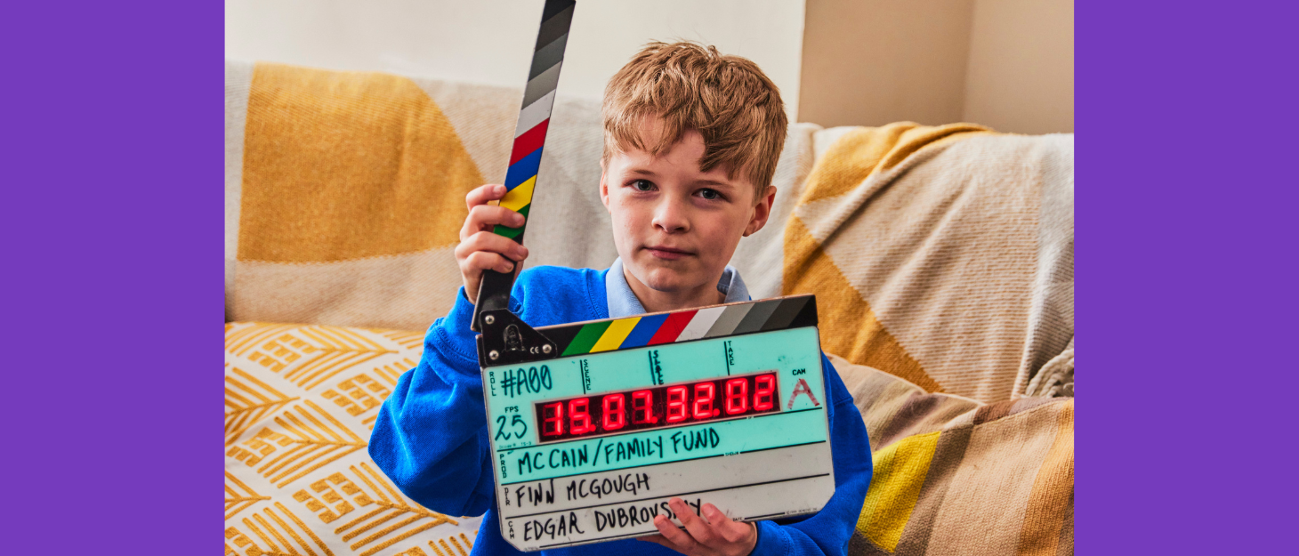 Boy sits on sofa holding a filming clapperboard