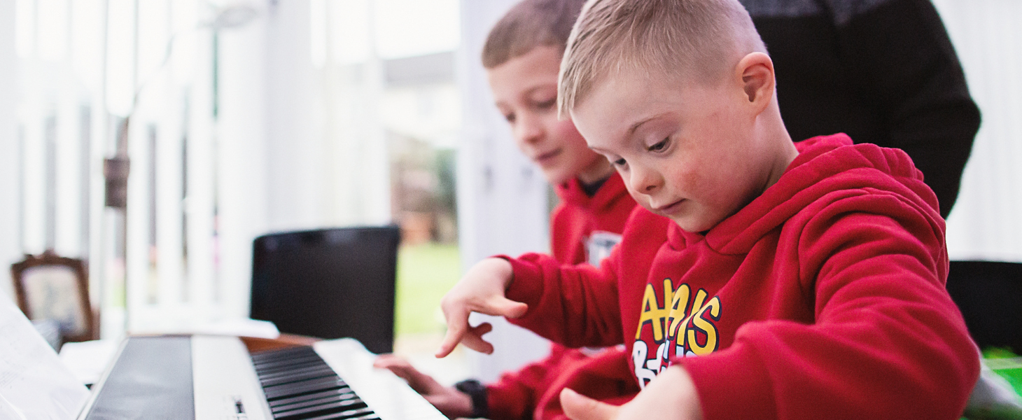 a boy wearing a red hoodie is playing the piano next to his brother and grandfather