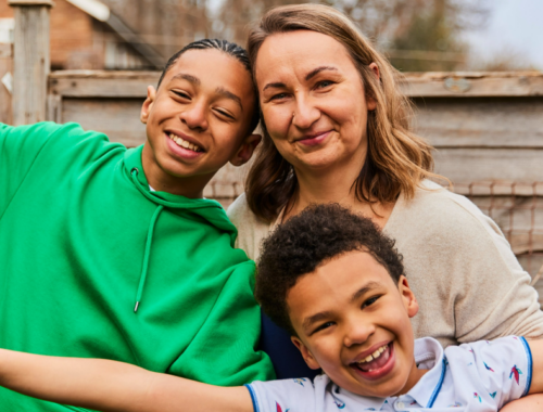 A mum and her two sons stand smiling together in their garden