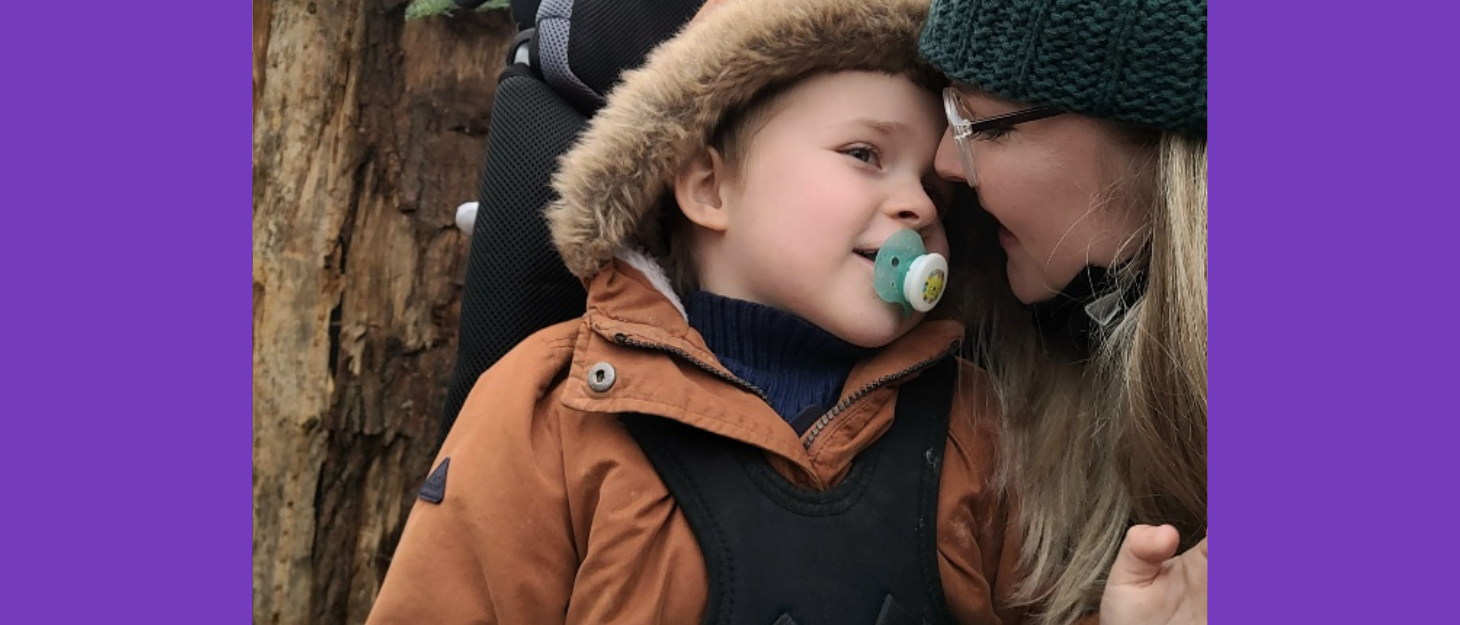 Mum leans down to kiss her son who is in a wheelchair on a cold day