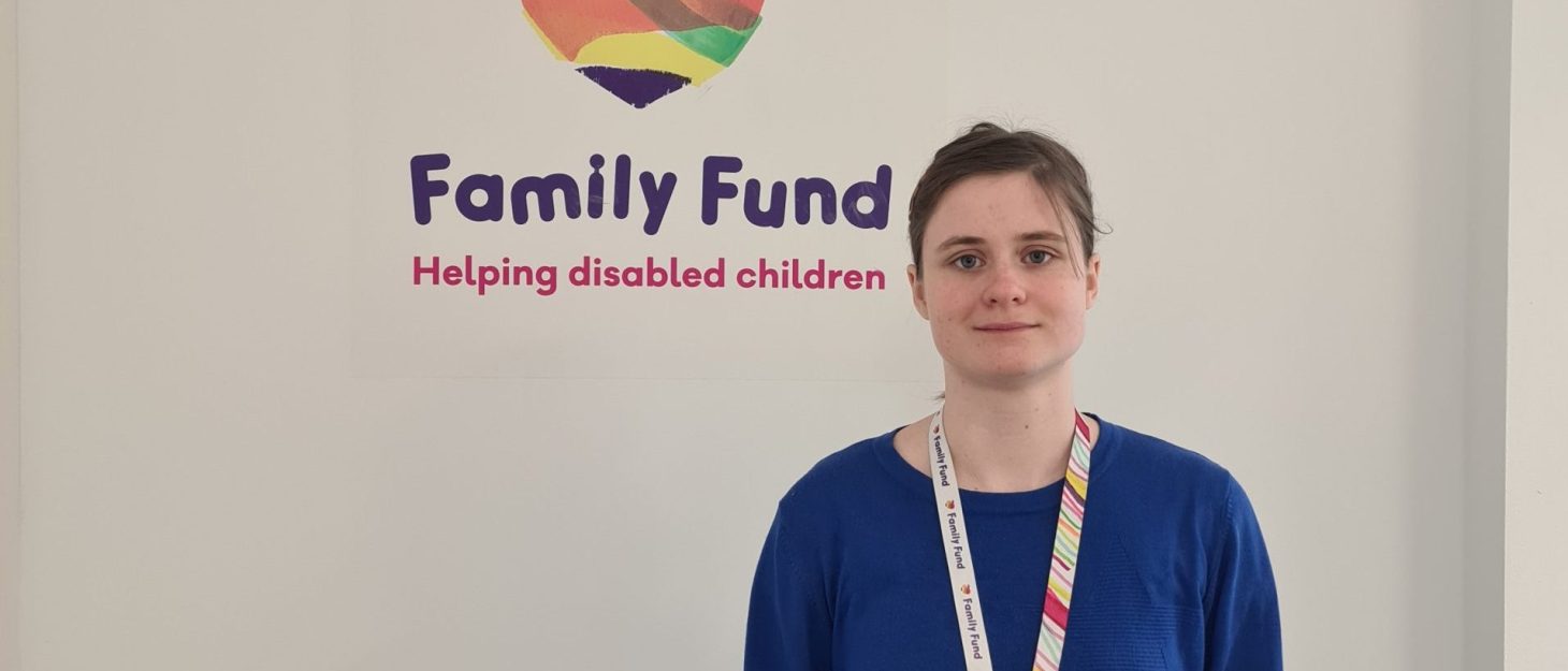 A supported intern, stands in front of a wall with the Family Fund logo on