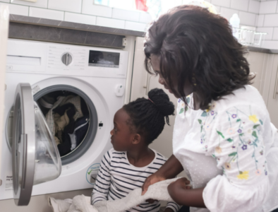 A girl and her mum load their washing machine together.